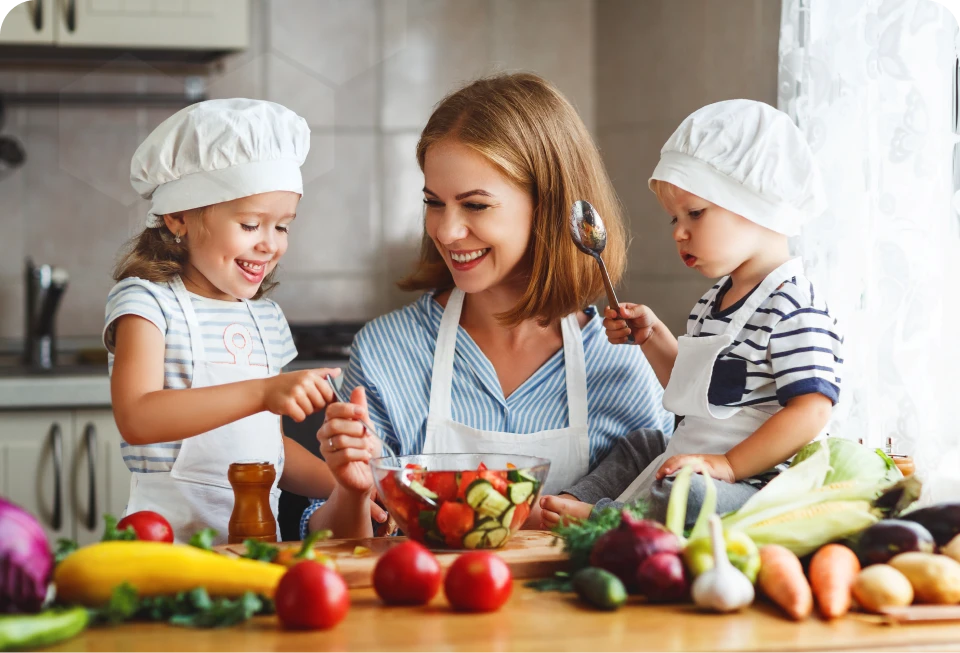 Mother and two young children preparing a fresh vegetable salad together in the kitchen.